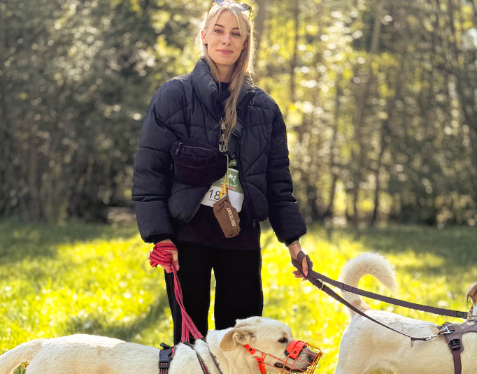 Eine Frau mit zwei Hunden an jeweils einer Leine. Sie nimmt mit den beiden Hunden am Tierschutzlauf teil. Beide Hunde haben ein helles Fell.
