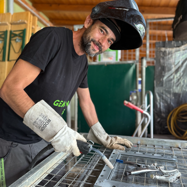 Mann mit kurzen Haaren kniet neben einem Hund im grünen Gras.