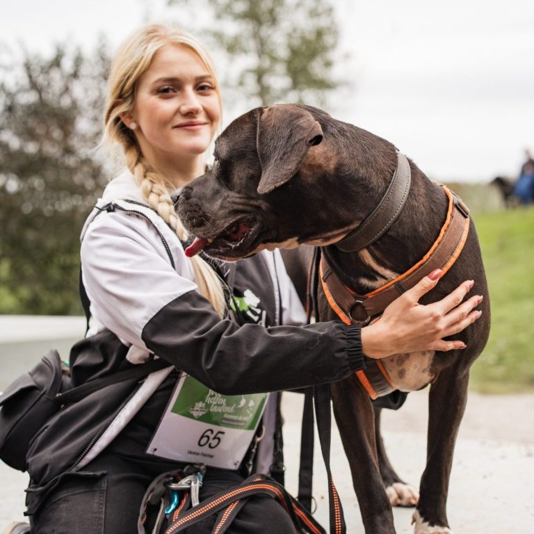 Frau mit langem Haar, die einen Tierschutz-Hund an der Leine hält, lächelt im Freien.