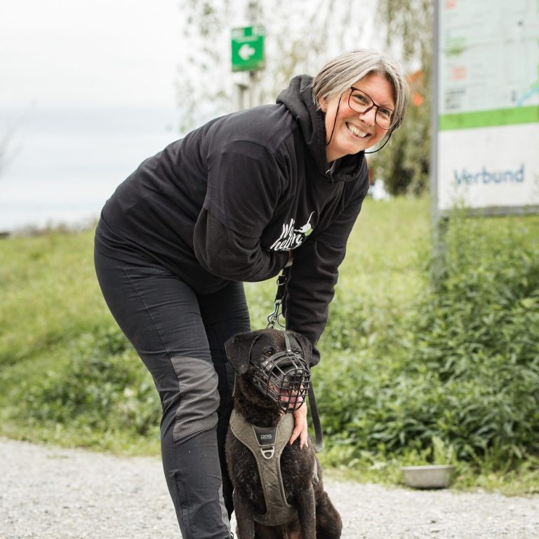 Frau mit Brille kniet neben einem Tierheim-Hund auf einem Weg im Freien. Tierschutz:läuft2024