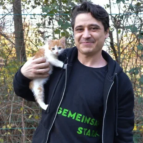 Mann mit kurzen Haaren kniet neben einem Hund im grünen Gras.