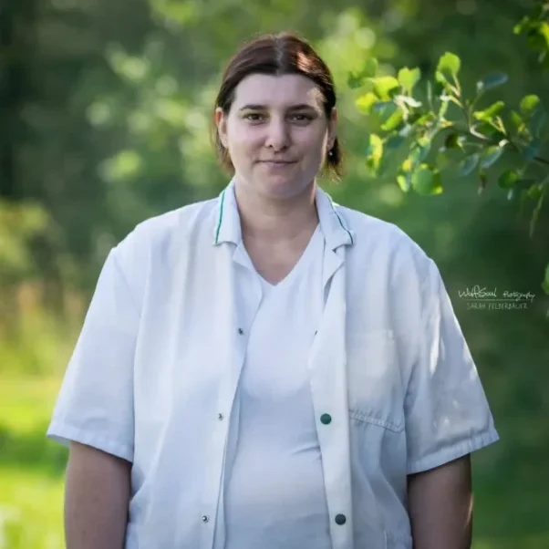 Mann mit kurzen Haaren kniet neben einem Hund im grünen Gras.