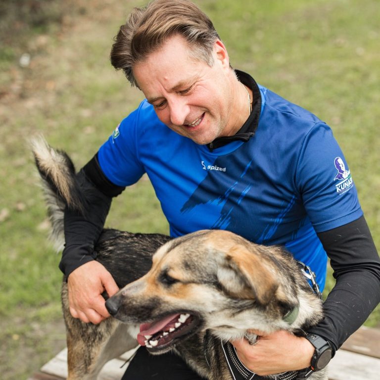 Mann mit blauer Sportbekleidung streichelt einen Tierheim-Hund im Freien. Tierschutz:läuft2024