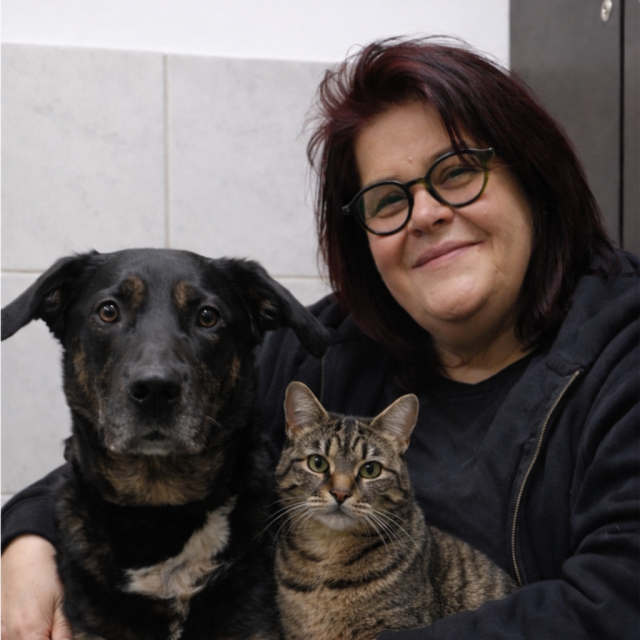 Mann mit kurzen Haaren kniet neben einem Hund im grünen Gras.